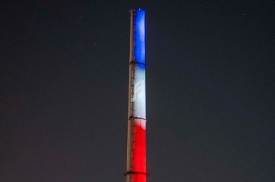 Cheminée industrielle éclairée en bleu, blanc et rouge dans la nuit, symbolisant les couleurs du drapeau français.