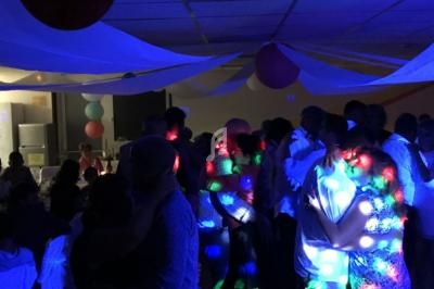 Des personnes dansent sous des lumières colorées dans une salle décorée avec des rubans et des ballons.