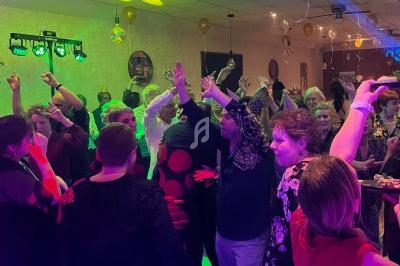 Des personnes dansent et lèvent les bras sur une piste éclairée par des lumières colorées lors d'une fête en intérieur.