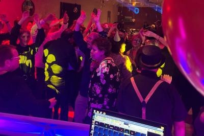 Groupe de personnes dansant sous des lumières colorées lors d'une soirée festive en intérieur.