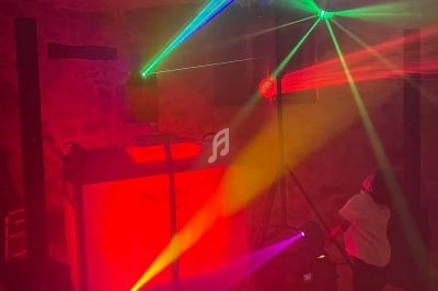 Jeu de lumières colorées avec lasers et projecteurs éclairant une salle sombre équipée d'un stand de DJ.