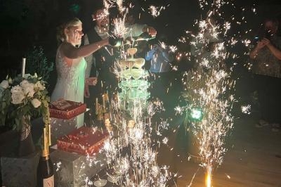 Une mariée verse du champagne dans une pyramide de verres entourée de feux d'artifice et de décorations festives.