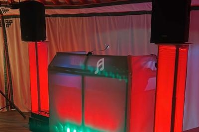 Un pupitre éclairé en rouge et vert, entouré de haut-parleurs noirs, dans une salle avec rideaux blancs.