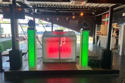 Stand de DJ avec éclairage LED rouge et vert, installé dans une salle avec décoration intérieure et lumière naturelle.
