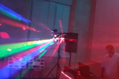 Effets lumineux colorés projetés dans une salle sombre avec un DJ à côté de son équipement.
