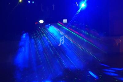 Jeu de lumières colorées et fumée dans une ambiance de soirée avec un DJ en arrière-plan.