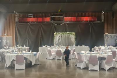 Salle de réception décorée avec des tables rondes dressées pour un événement, un enfant marche au centre.