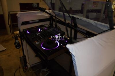 Console DJ équipée de platines et d'un micro, installée dans un espace intérieur avec une protection en plexiglas.