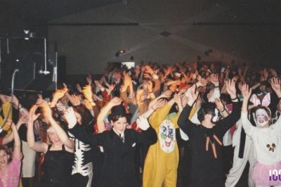 Personnes déguisées levant les bras lors d'une fête ou d'un événement festif dans une salle bondée.