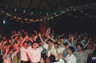 Groupe de personnes dansant sous des guirlandes lumineuses dans une salle à l'ambiance festive.