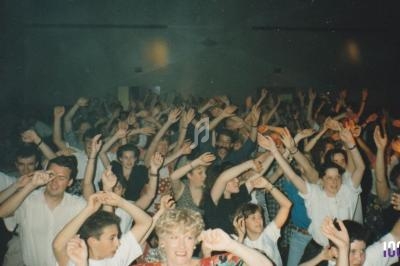 Groupe de personnes levant les bras et dansant dans une salle sombre lors d'un événement festif.