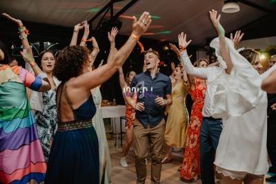 Des personnes dansent et lèvent les bras lors d'une fête dans une salle éclairée avec des lumières colorées.