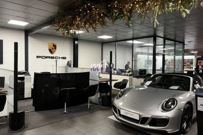 Salle d'exposition automobile avec une Porsche grise cabriolet au premier plan et un bureau en arrière-plan.