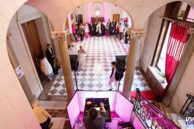 Vue plongeante sur une réception dans un hall élégant avec carrelage en damier, invités et DJ en arrière-plan.