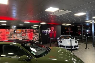 Exposition de voitures Porsche dans un showroom moderne avec éclairage tamisé et panneaux décoratifs.