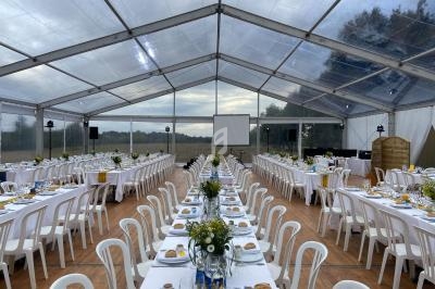 Grande tente transparente aménagée avec des tables longues décorées de fleurs et dressées pour un événement.