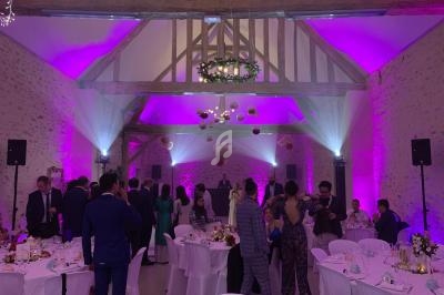 Salle de réception en pierre avec poutres apparentes, éclairée par des lumières violettes, des invités discutent autour des…