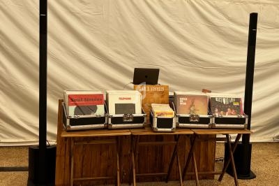 Stand avec des vinyles exposés dans des bacs en bois, un ordinateur portable et des enceintes en arrière-plan.