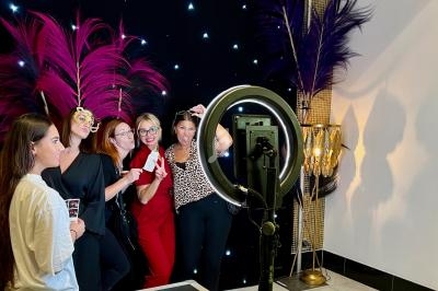 Des personnes posent devant un décor festif avec des plumes colorées et un éclairage de studio.