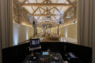 Salle de réception décorée avec des guirlandes lumineuses, vue depuis une table de mixage avec équipement DJ.
