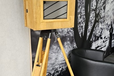 Borne photo en bois sur trépied, équipée d'un objectif et d'un écran, installée dans un espace intérieur.