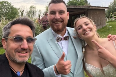 Trois personnes souriantes posent à l'extérieur devant un bâtiment en bois, dans un cadre verdoyant.