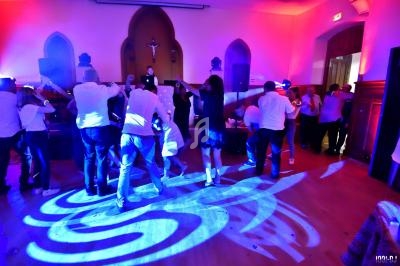 Des personnes dansent dans une salle éclairée par des lumières colorées, avec un DJ en arrière-plan.