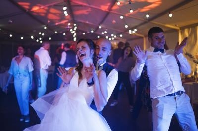 Un couple danse joyeusement lors d'une fête sous une tente éclairée de guirlandes lumineuses.