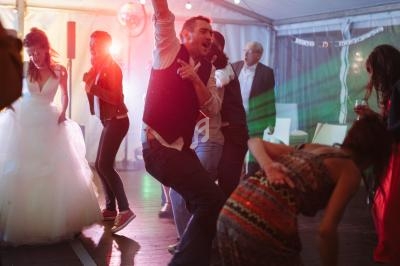 Personnes dansant sous une tente éclairée de guirlandes lumineuses, ambiance festive avec jeux de lumière colorés.