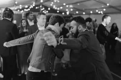 Deux personnes dansent face à face lors d'un événement festif sous une tente éclairée par des guirlandes lumineuses.