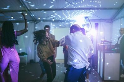 Des personnes dansent sous des lumières colorées dans une ambiance festive sous une tente.