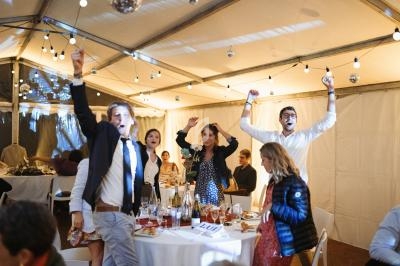 Des invités debout autour d'une table, levant les bras et célébrant dans une tente décorée de guirlandes lumineuses.