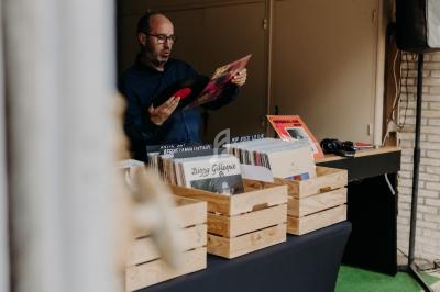 Un homme examine un disque vinyle près de bacs en bois contenant des albums dans un espace intérieur.