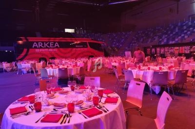 Salle de réception avec tables dressées pour un événement, un bus rouge Arkea Samsic visible en arrière-plan.