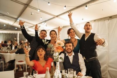 Groupe de personnes souriantes levant leurs verres dans une salle de réception décorée avec des guirlandes lumineuses.