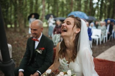 Un couple assis lors d'une cérémonie de mariage en extérieur, la mariée riant joyeusement.