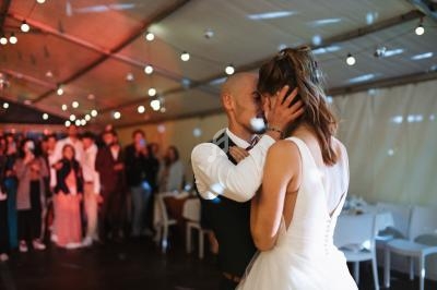 Un couple danse tendrement sous une tente éclairée, entouré d'invités en arrière-plan flou.
