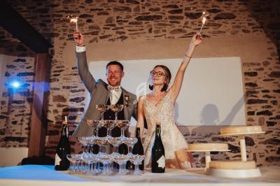 Un couple souriant lève des cierges magiques près d'une pyramide de coupes de champagne lors d'une célébration.