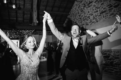 Un couple danse joyeusement dans une salle en pierre avec des invités en arrière-plan.