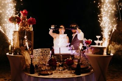 Un couple célèbre son mariage devant un gâteau illuminé, entouré de décorations et de feux d'artifice.