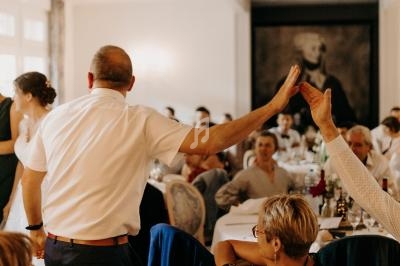 Un homme en chemise blanche fait un high-five avec une personne assise dans une salle de réception animée.