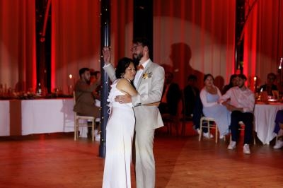 Un couple danse sous un éclairage tamisé dans une salle avec des invités assis en arrière-plan.