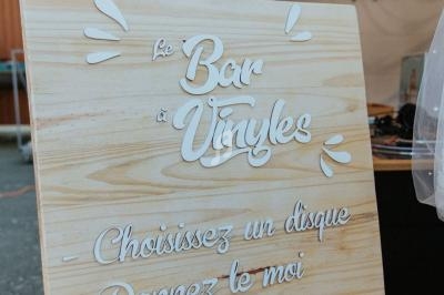 Panneau en bois avec l'inscription ’Le Bar à Vinyles’ devant un stand sous une tente.