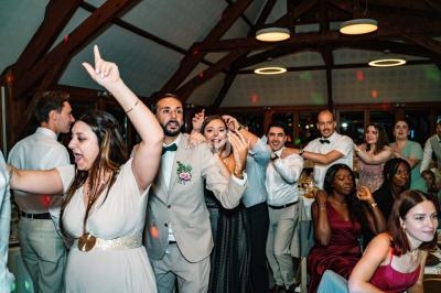 Des invités dansent et célèbrent dans une salle avec charpente en bois, éclairée par des suspensions circulaires.