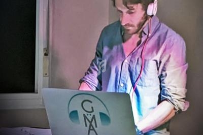 Homme portant un casque audio, concentré sur un ordinateur portable dans une pièce faiblement éclairée.