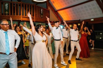 Des personnes dansent en groupe dans une salle éclairée, certaines en tenue élégante, souriantes et synchronisées.