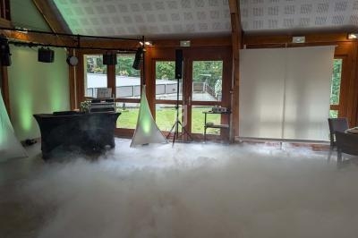 Salle de réception avec éclairage d'ambiance, fumée au sol et vue sur un espace extérieur verdoyant.