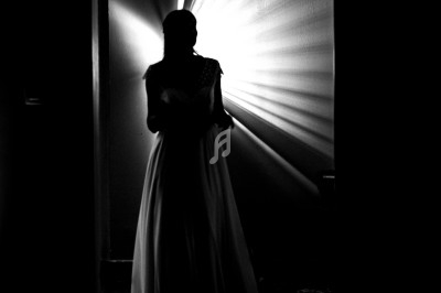 Silhouette d'une femme en robe longue, éclairée par une lumière rayonnante dans un couloir sombre.