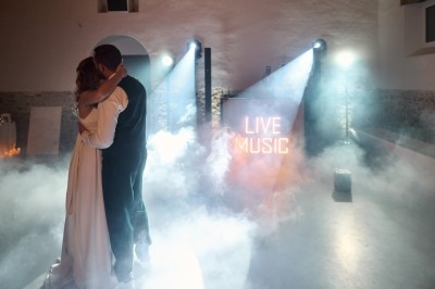 Un couple danse dans une ambiance tamisée avec des lumières et de la fumée, un panneau ’Live Music’ en arrière-plan.
