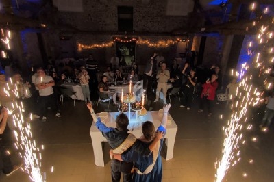 Un couple de dos célèbre un événement devant une table décorée, entouré d'invités et de gerbes d'étincelles.